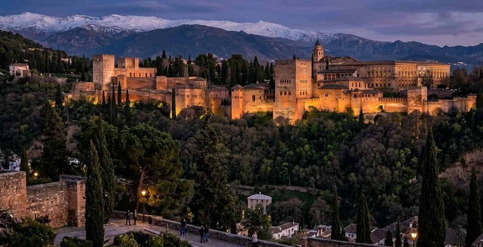 The Alhambra palace complex at dusk against the Sierra Nevada mountains