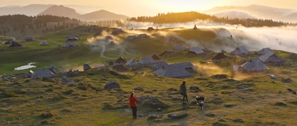 Velika Planina sunrise, fog through huts, two people and a dog